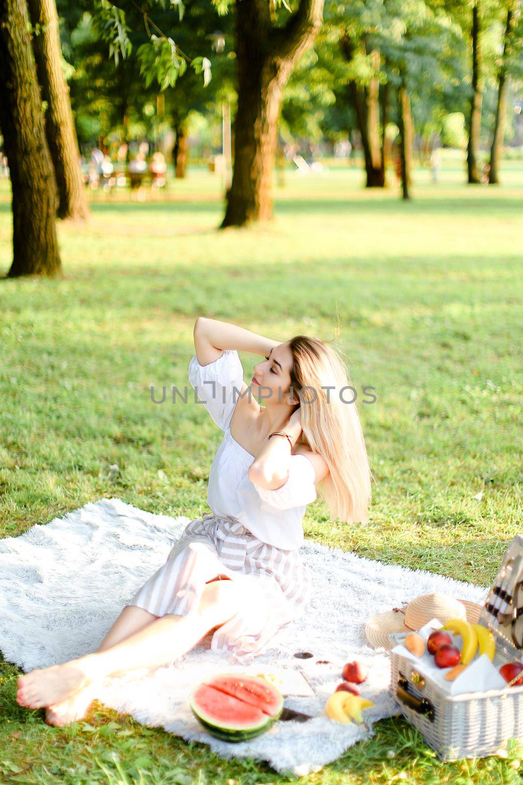 Young woman sitting on plaid with fruits in park. by sisterspro