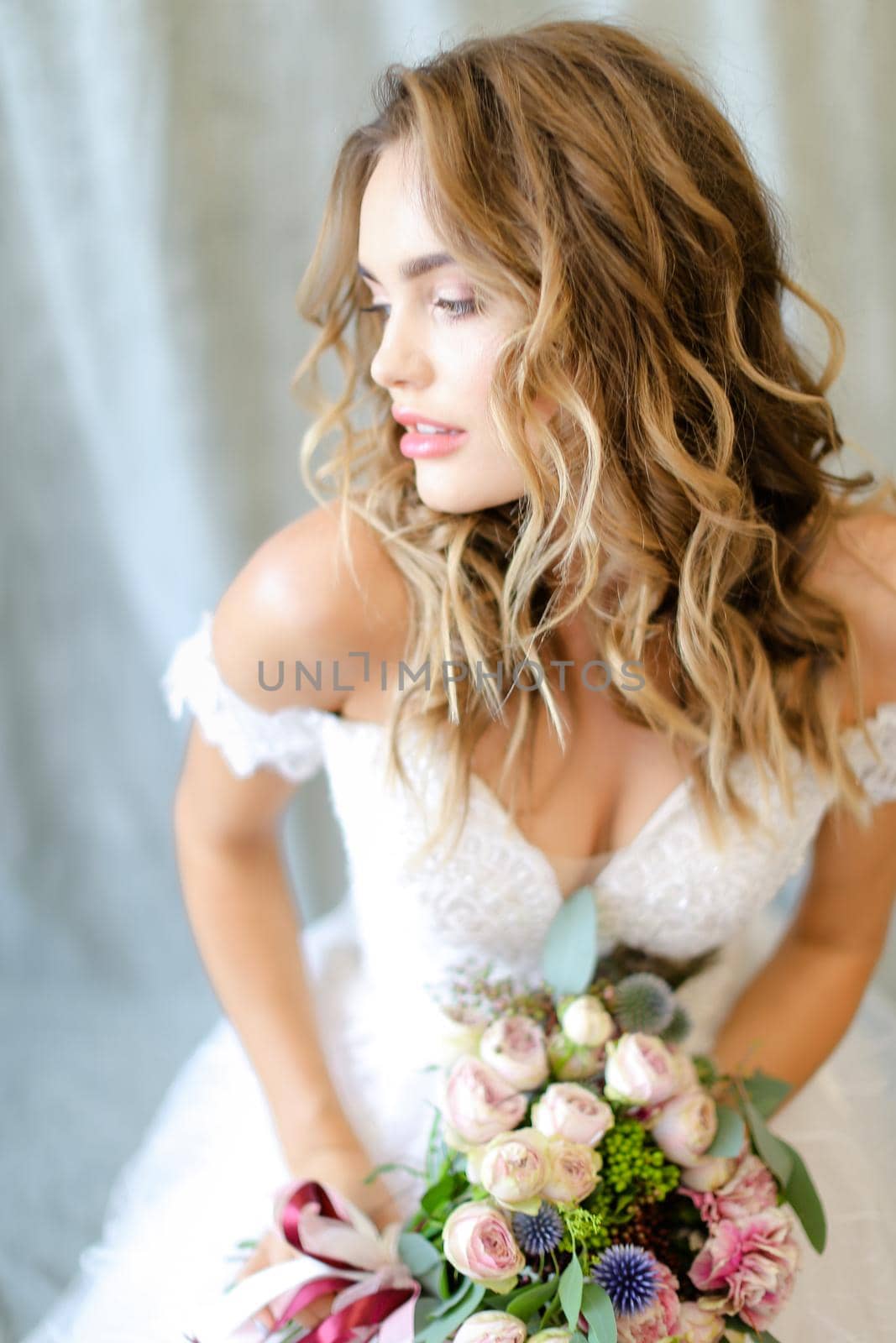 Young beautiful bride wearing white dress with bouquet at photo studio. Concept of bridal photo session, wedding and floristic art.