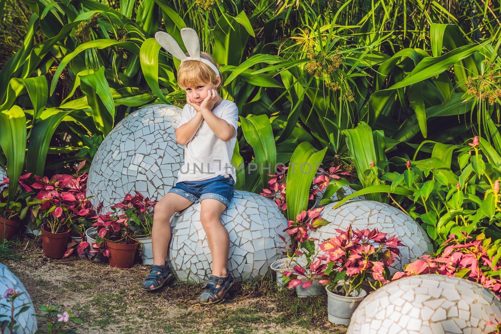 Cute little kid boy with bunny ears having fun with traditional Easter eggs hunt, outdoors. Celebrating Easter holiday. Toddler finding, colorful eggs.