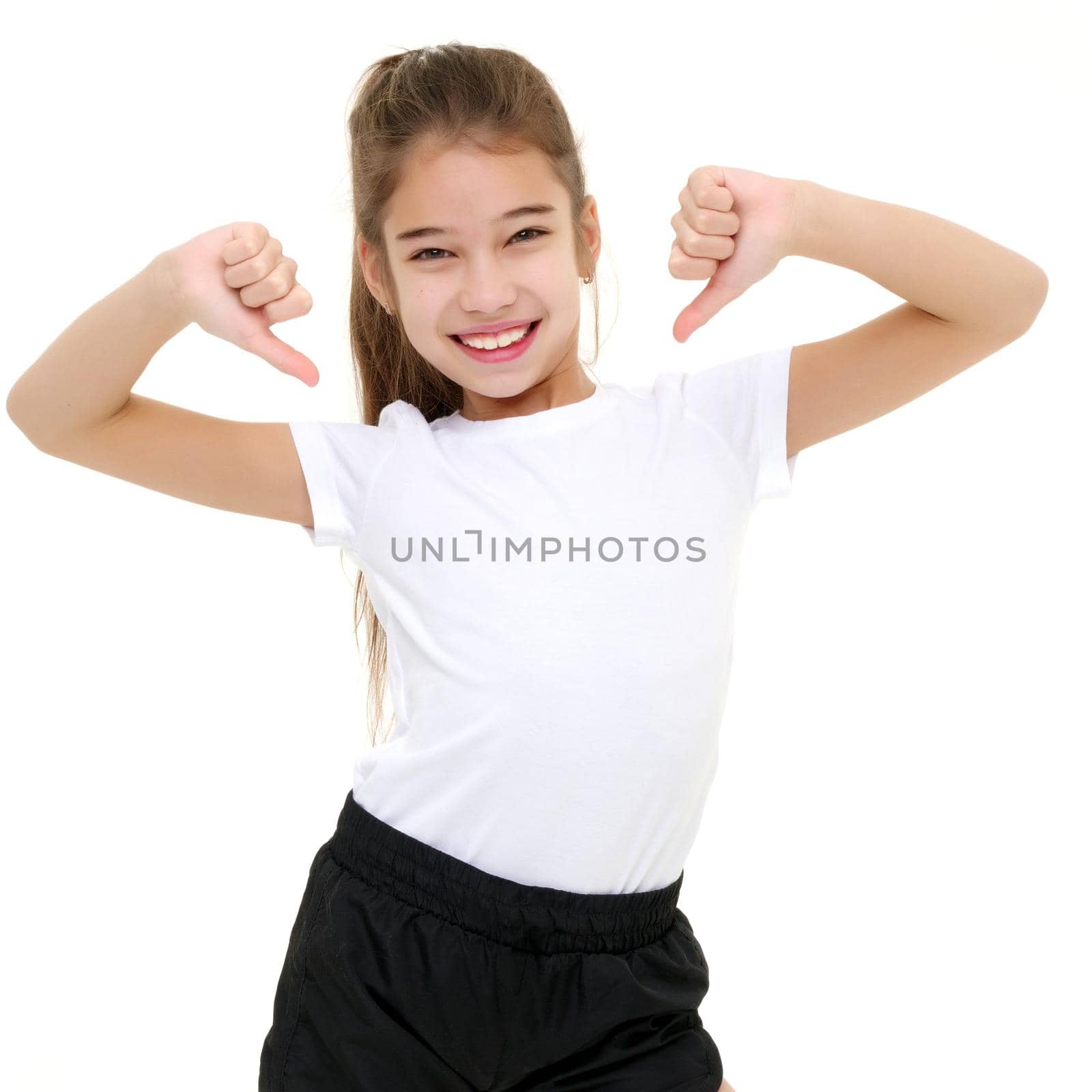A beautiful little girl in an empty white T-shirt points to herself. The concept of design of T-shirts, advertising of children's goods. Isolated on white background.