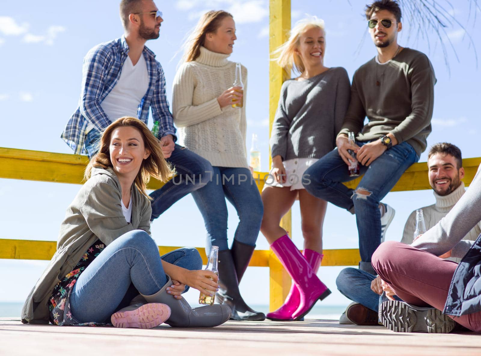 Happy Group Of Friends Hanging Out At Beach House having fun and drinking beer on autumn day