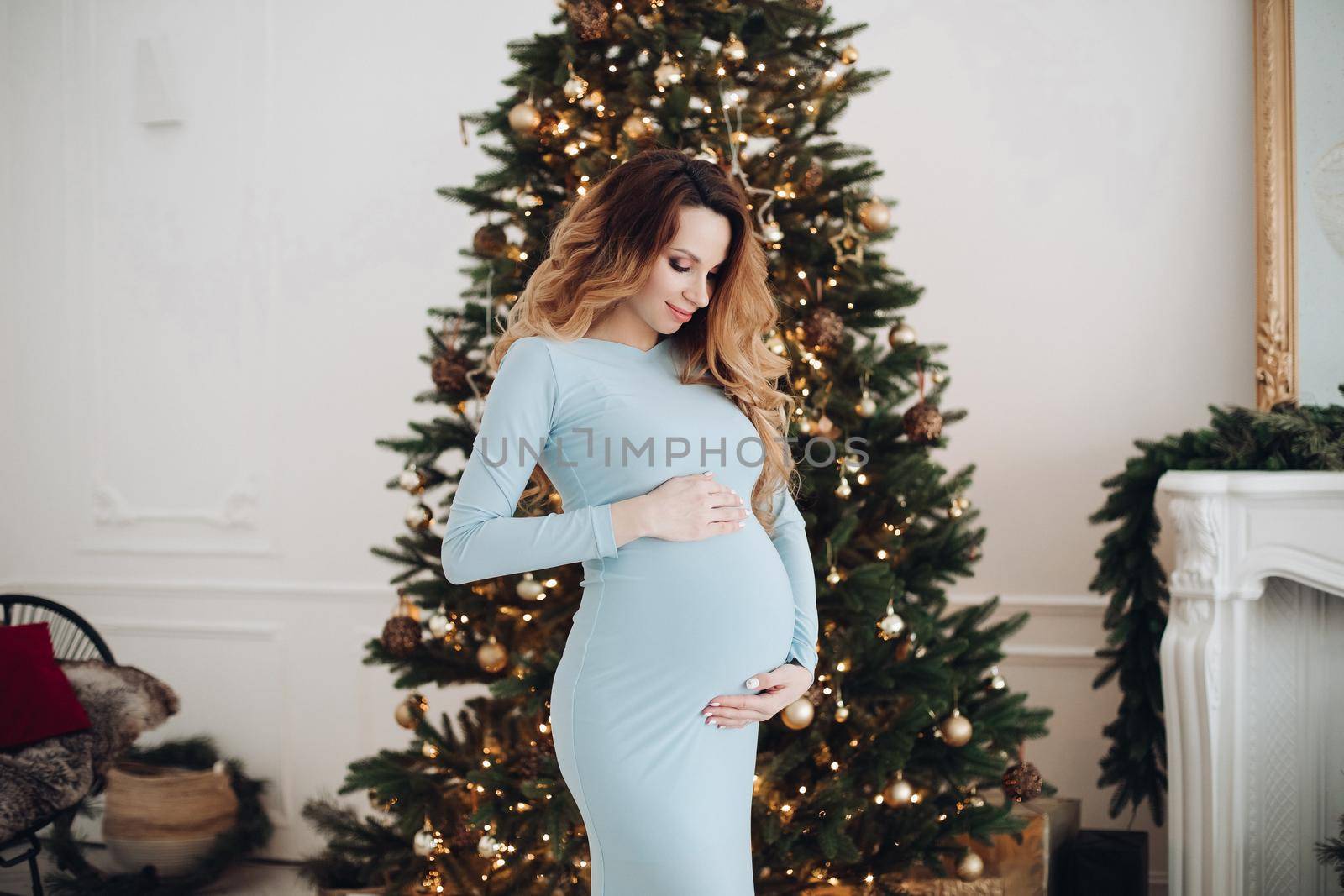 Young pregnant woman poses for the camera in long blue dress in christmas atmosphere