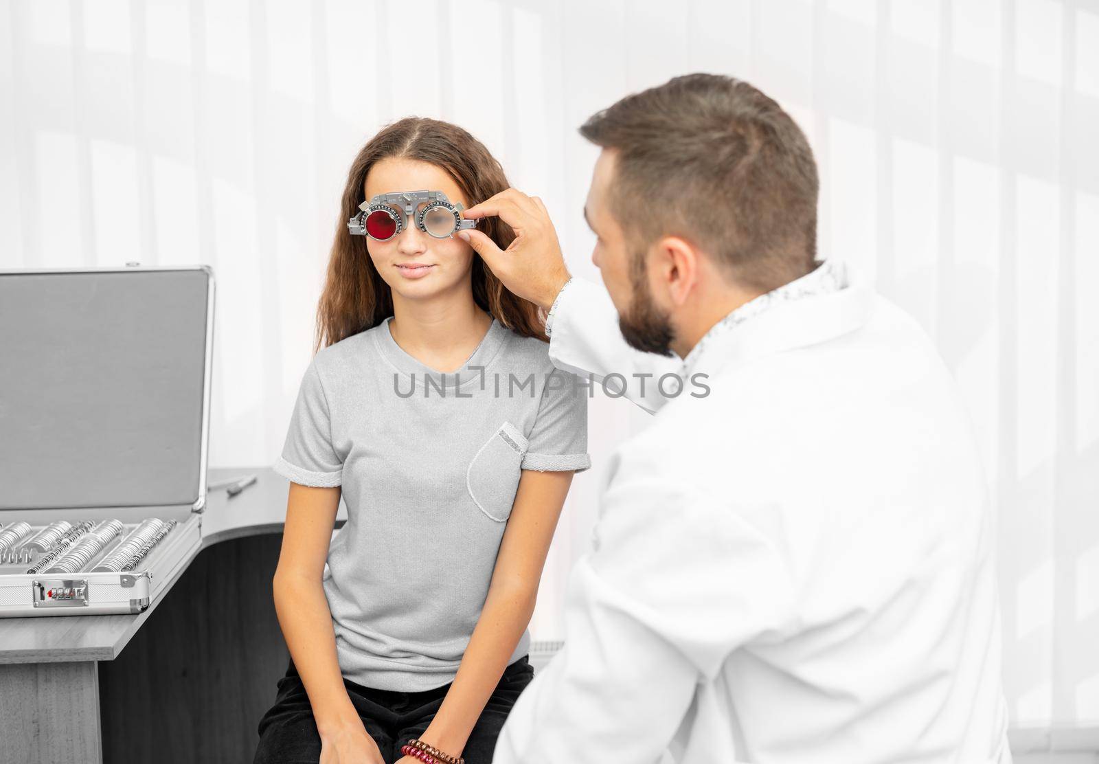 Doctor ophthalmologist holding special eye equipment examinating teenager girl's eyes in the clinic