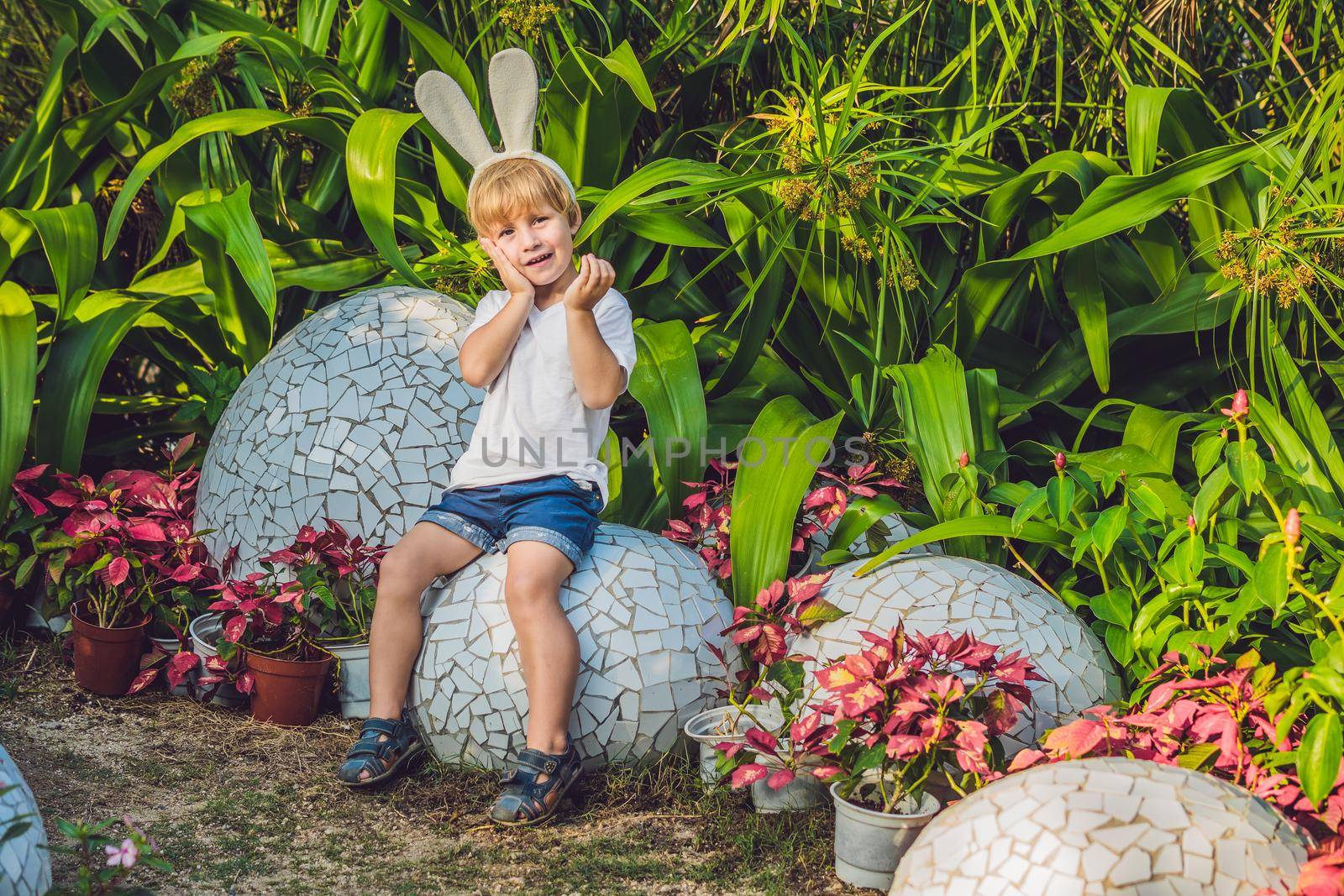 Cute little kid boy with bunny ears having fun with traditional Easter eggs hunt, outdoors. Celebrating Easter holiday. Toddler finding, colorful eggs.