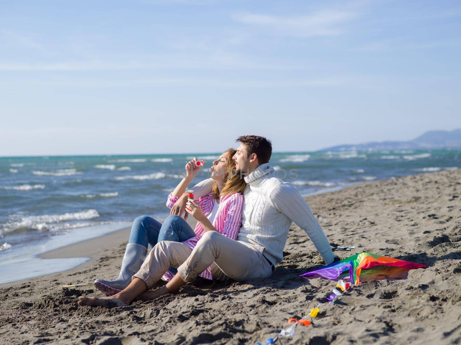 Young Couple having fun and making soap bubbles On The Beach at autumn day