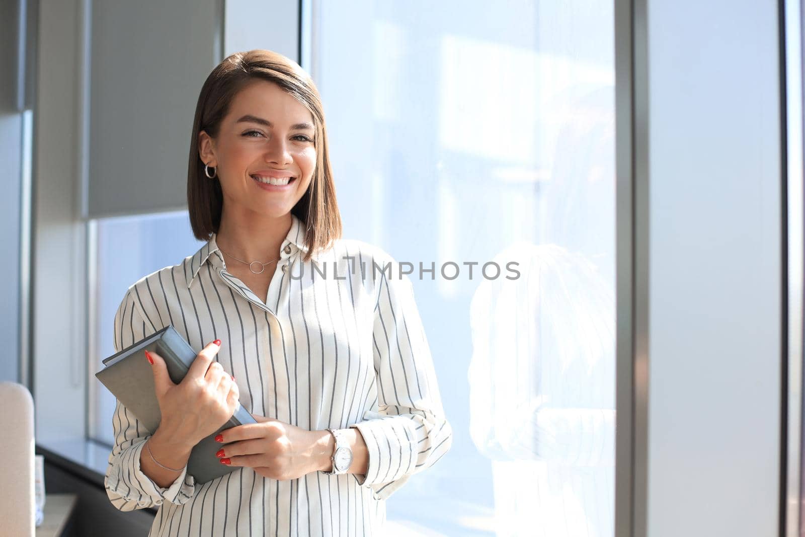 Attractive business woman looking at camera and smiling while standing in the office. by tsyhun