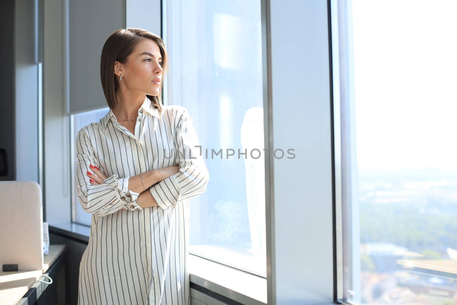 Attractive business woman in smart casual wear looking away and smiling while standing in the office.