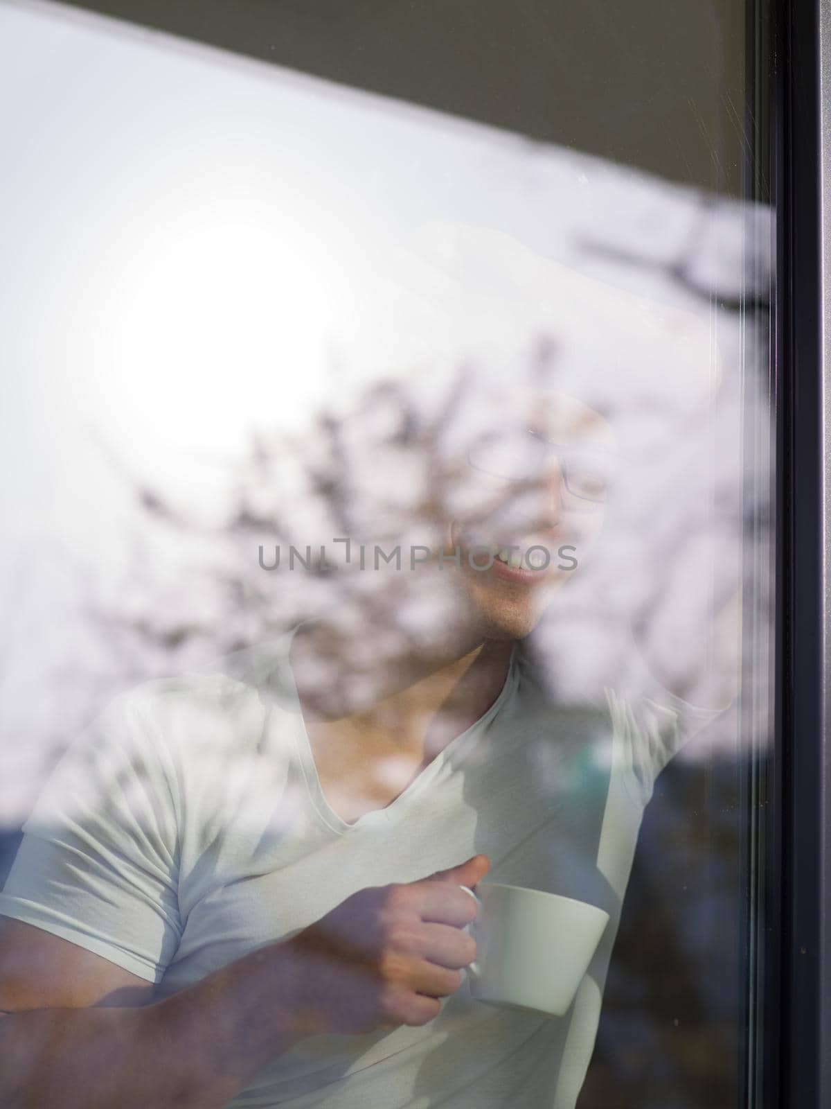 young handsome man drinking morning coffee by the window in his home