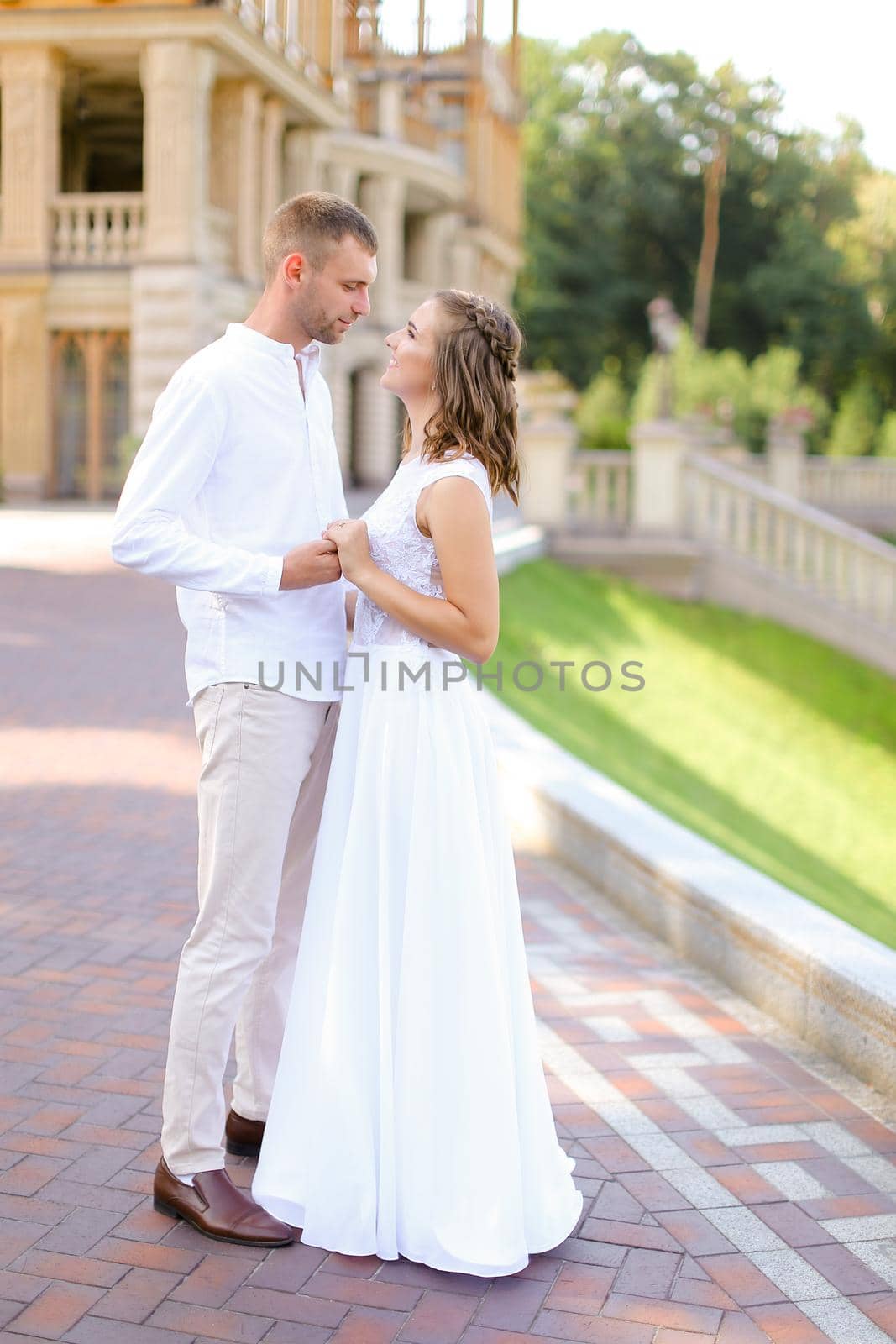 Happy young bride and groom holding hands and standing outdoors. Concept of relationship, wedding and bridal photo session.