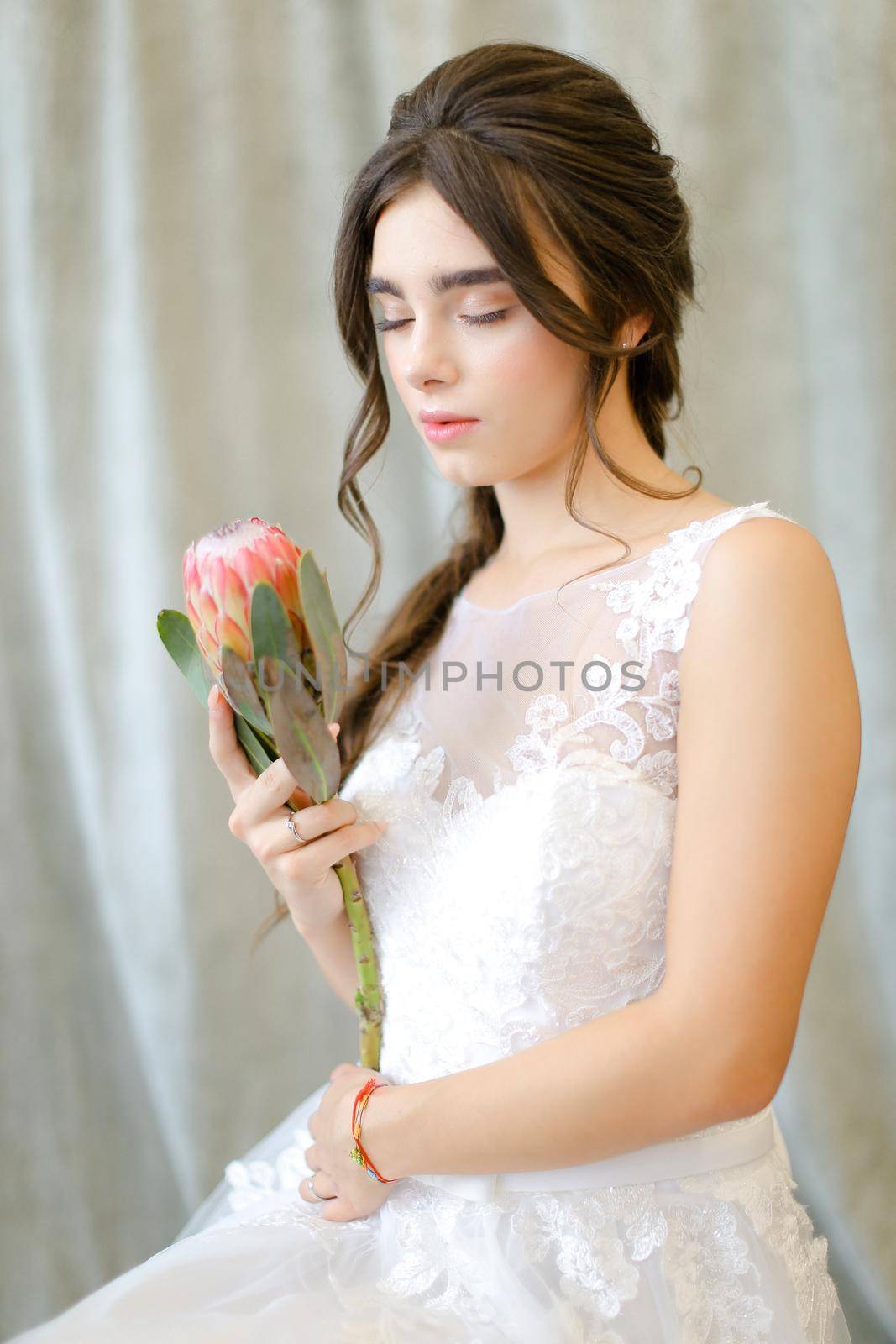 Portrait of beautiful brunette caucasian bride with flowers at studio. Concept of bridal photo session and bridal makeup.