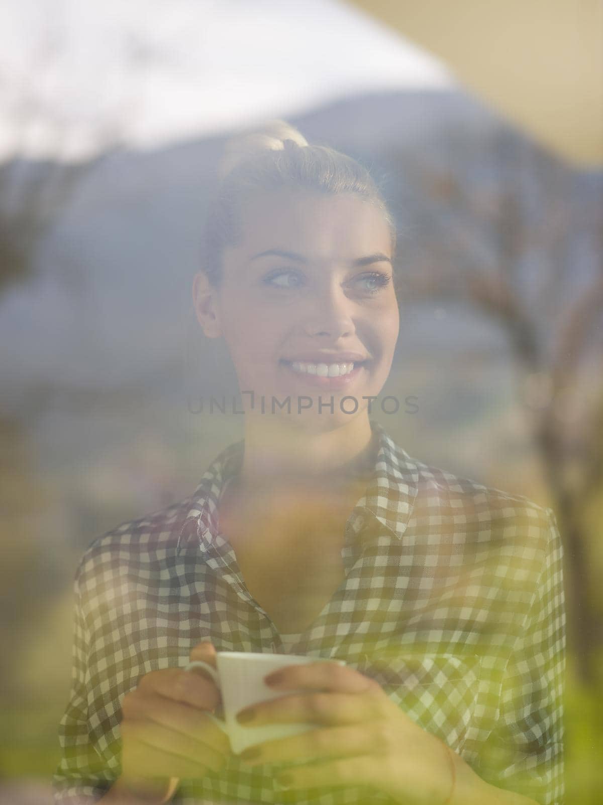 beautiful young woman drinking morning coffee by the window in her home