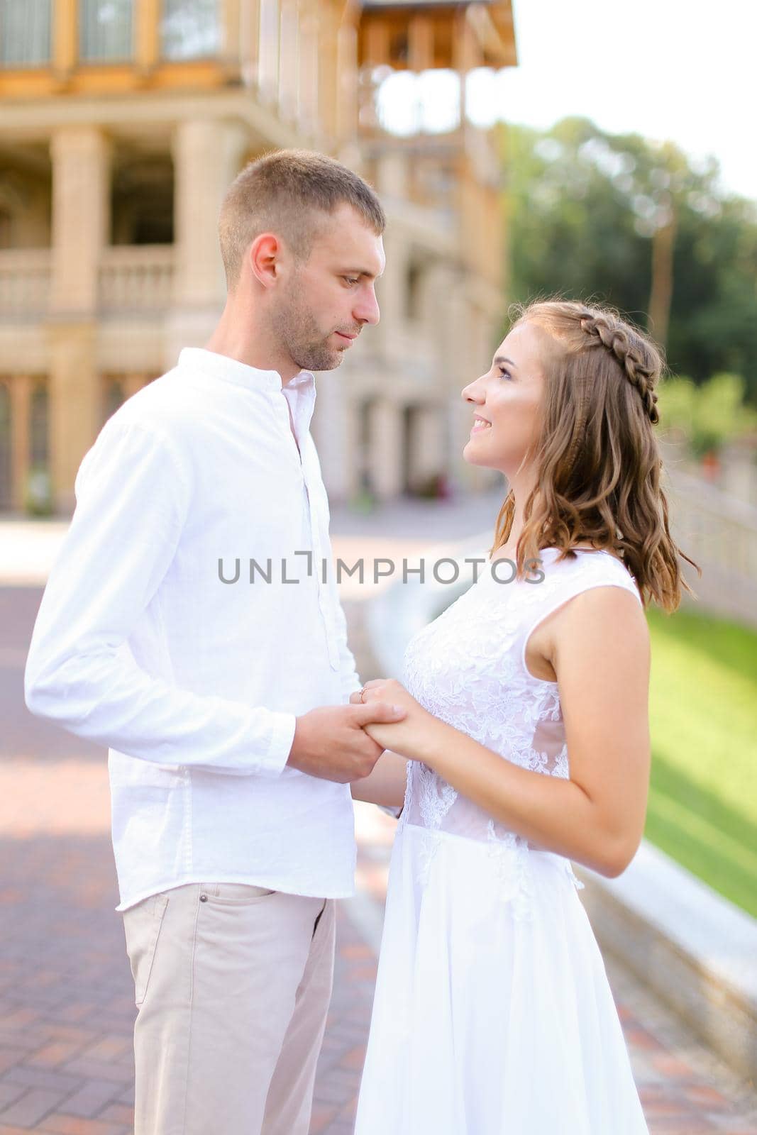 Happy bride and groom holding hands and standing outdoors. Concept of relationship, wedding and bridal photo session.