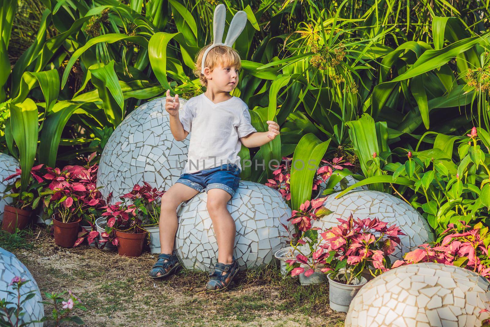Cute little kid boy with bunny ears having fun with traditional Easter eggs hunt, outdoors. Celebrating Easter holiday. Toddler finding, colorful eggs by galitskaya
