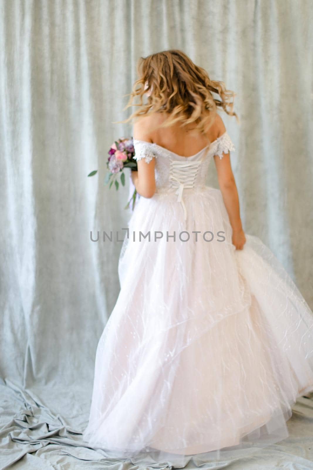 Back view of young bride standing at studio with flowers. Concept of wedding and bridal photo sesion, fashion.