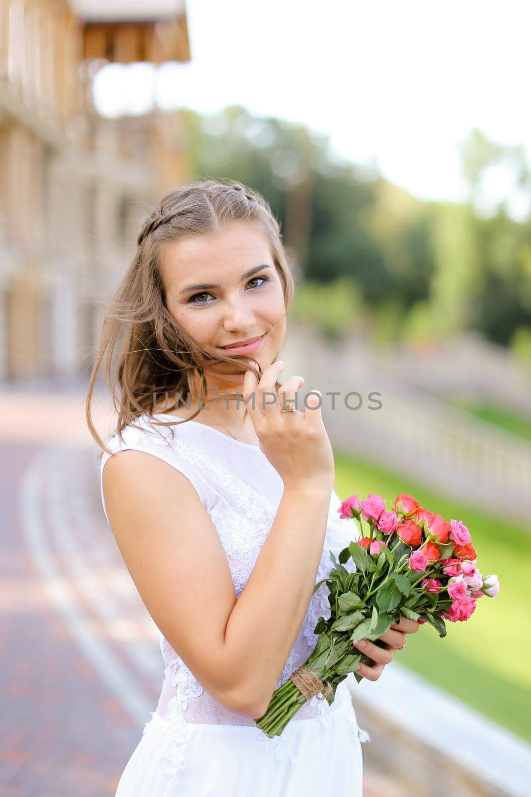 Young blonde bride wearing white dress and standing outside with flowers. by sisterspro