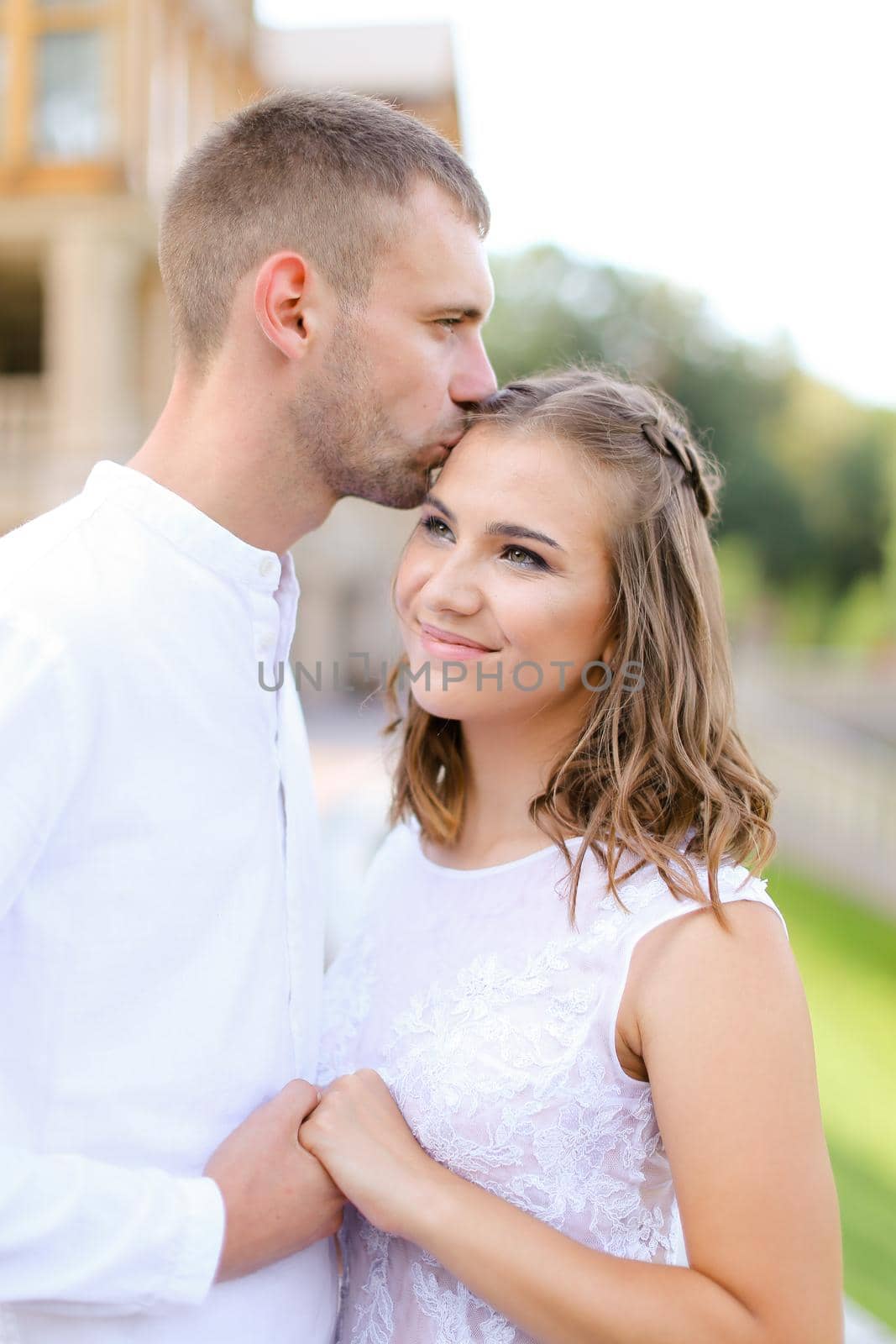 Caucasian groom kissing bride and holding hands outside. by sisterspro