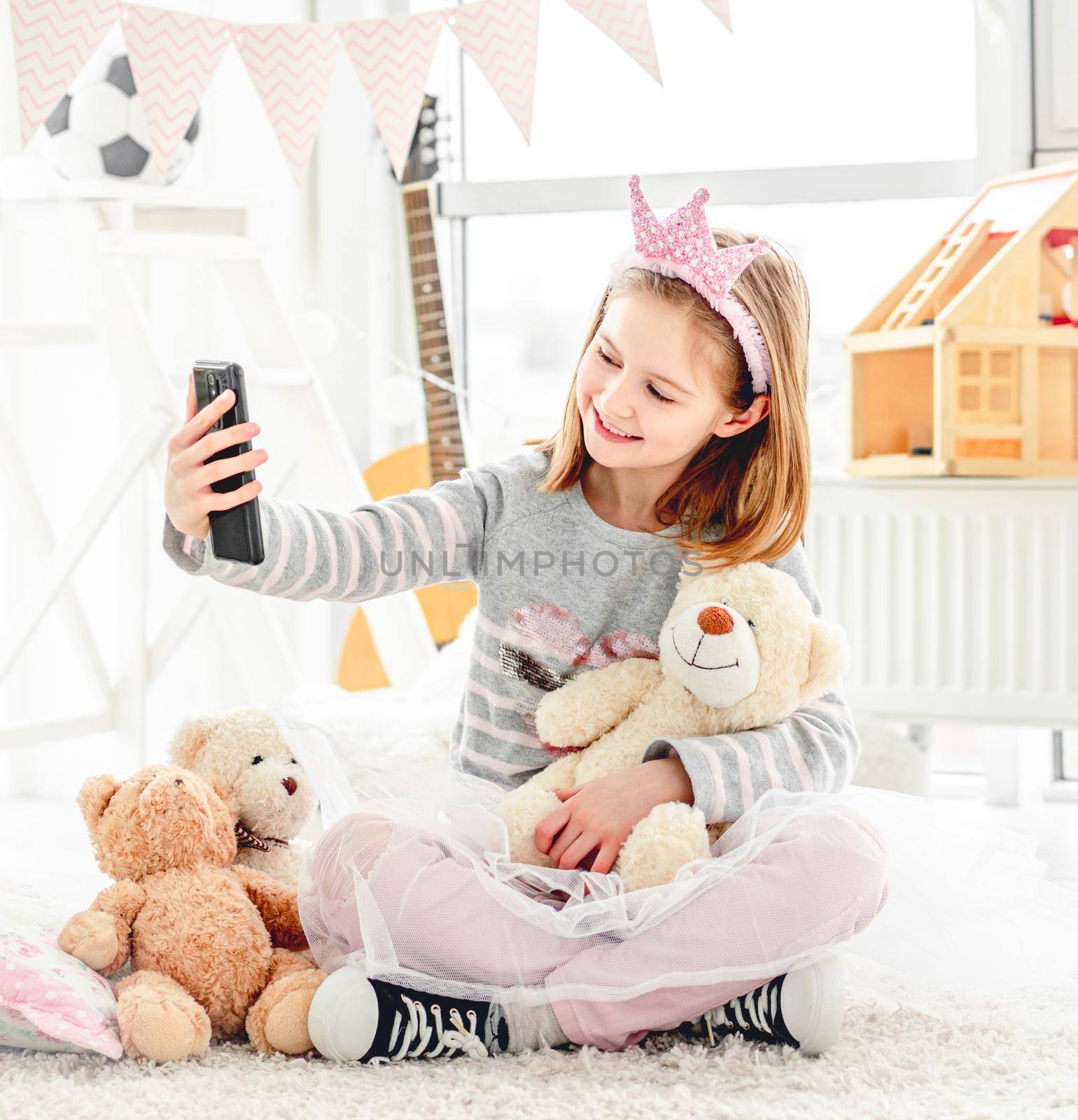 Cute little girl taking selfie with teddy bear in light room