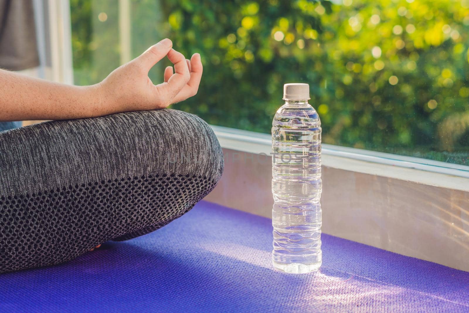 hand of a woman meditating in a yoga pose on a rug for yoga and a bottle of water by galitskaya