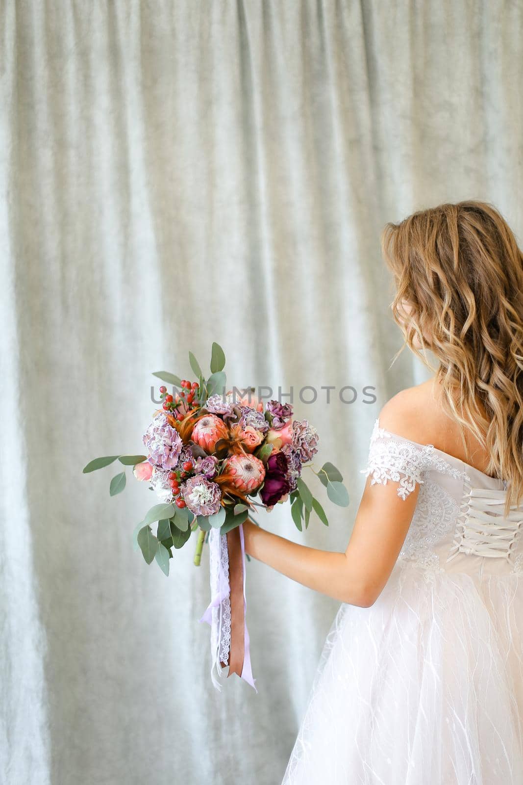 Back view of young caucasian bride standing at studio with flowers. Concept of wedding and bridal photo sesion, fashion.