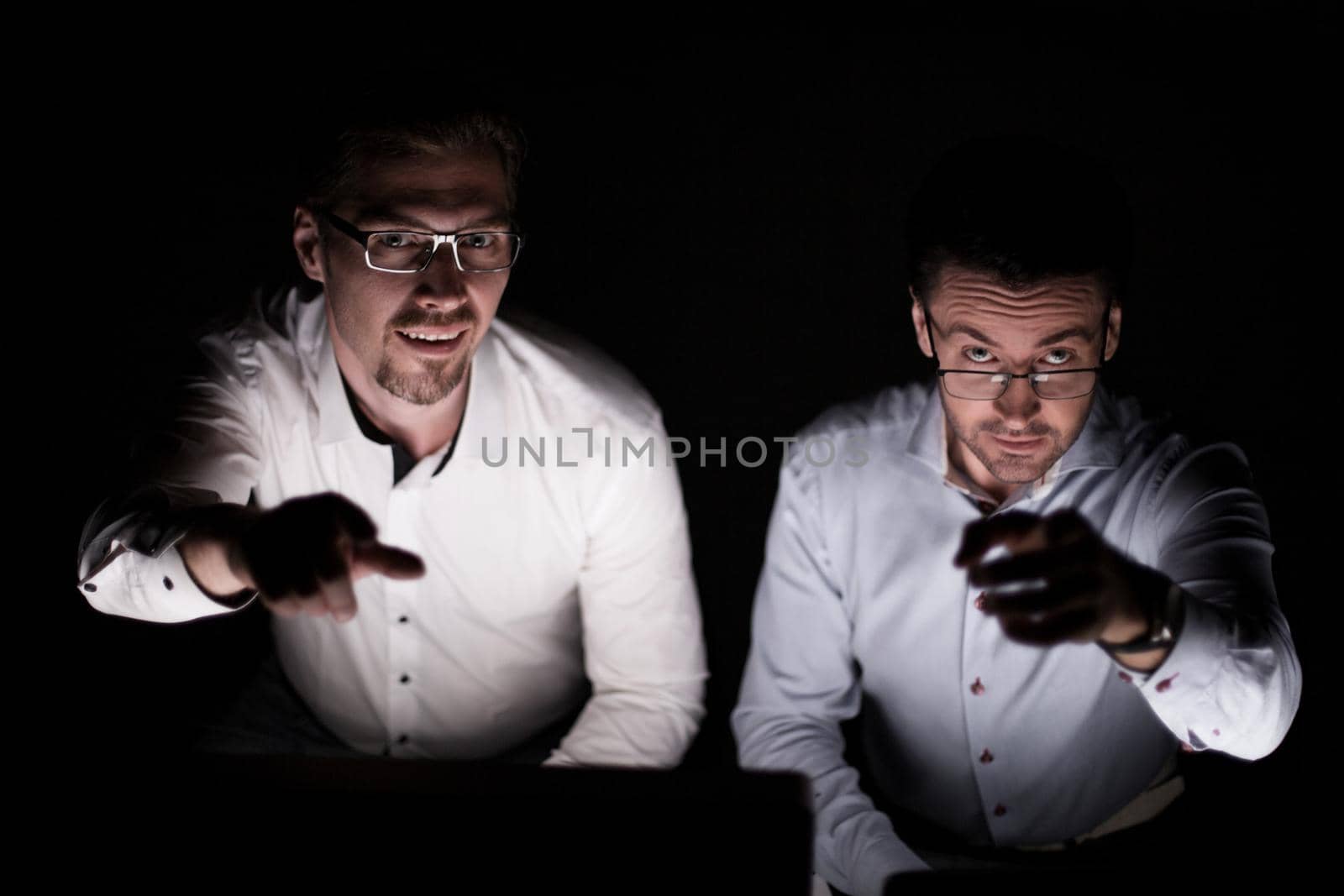 close up.two colleagues sitting at their Desk and pointing at you.isolated on black