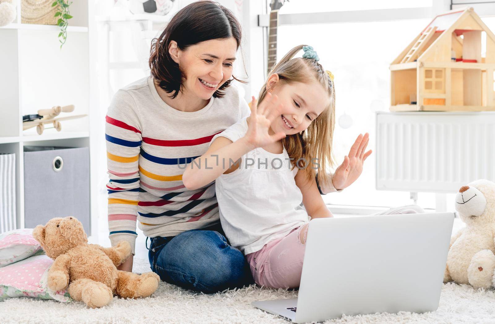 Cute little girl with pretty mother doing video calling on laptop in cozy children room