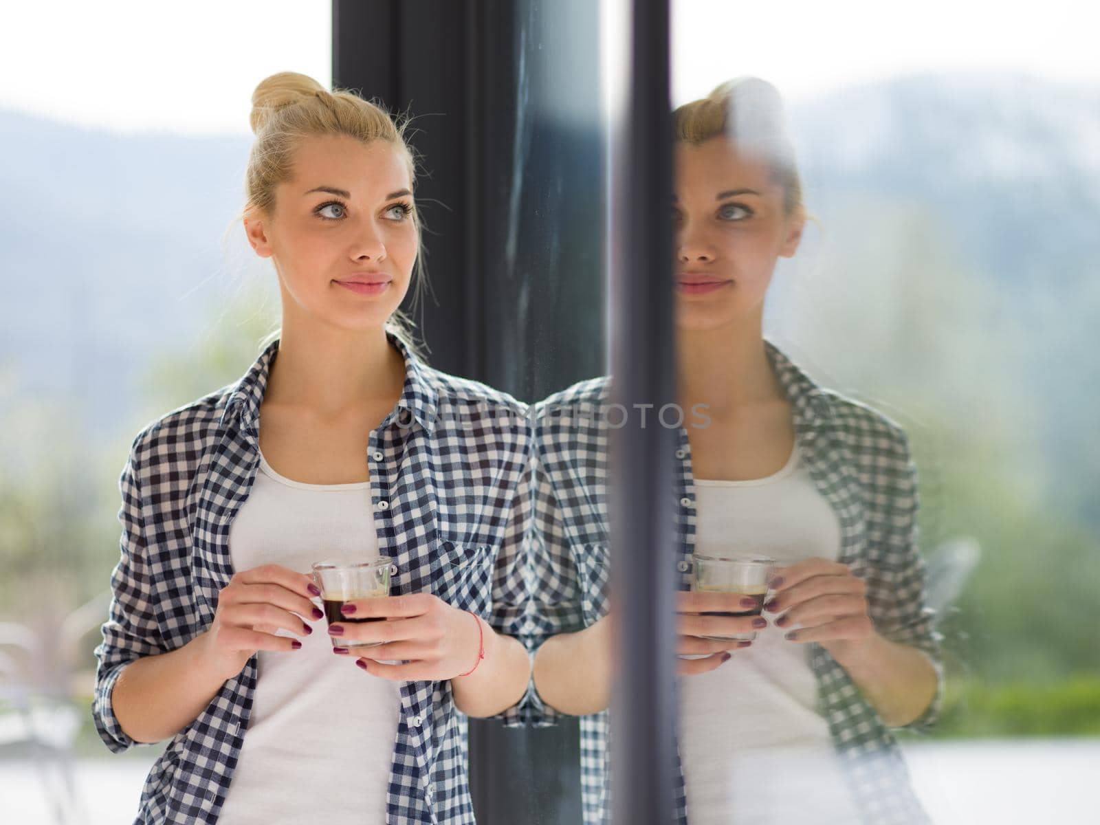 beautiful young woman drinking morning coffee by the window in her home