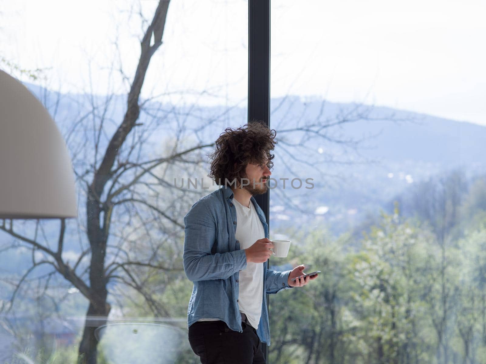 Handsome casual young man drinking coffee and using a mobile phone at  home