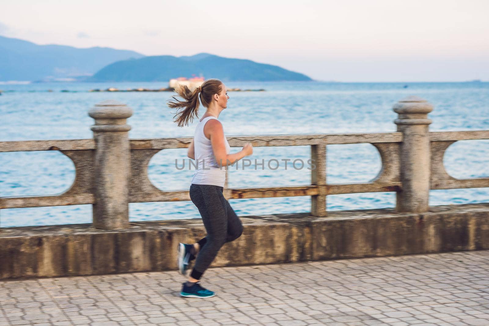 Athletic girl on seafront. Young sportswoman doing exercises against the sea.