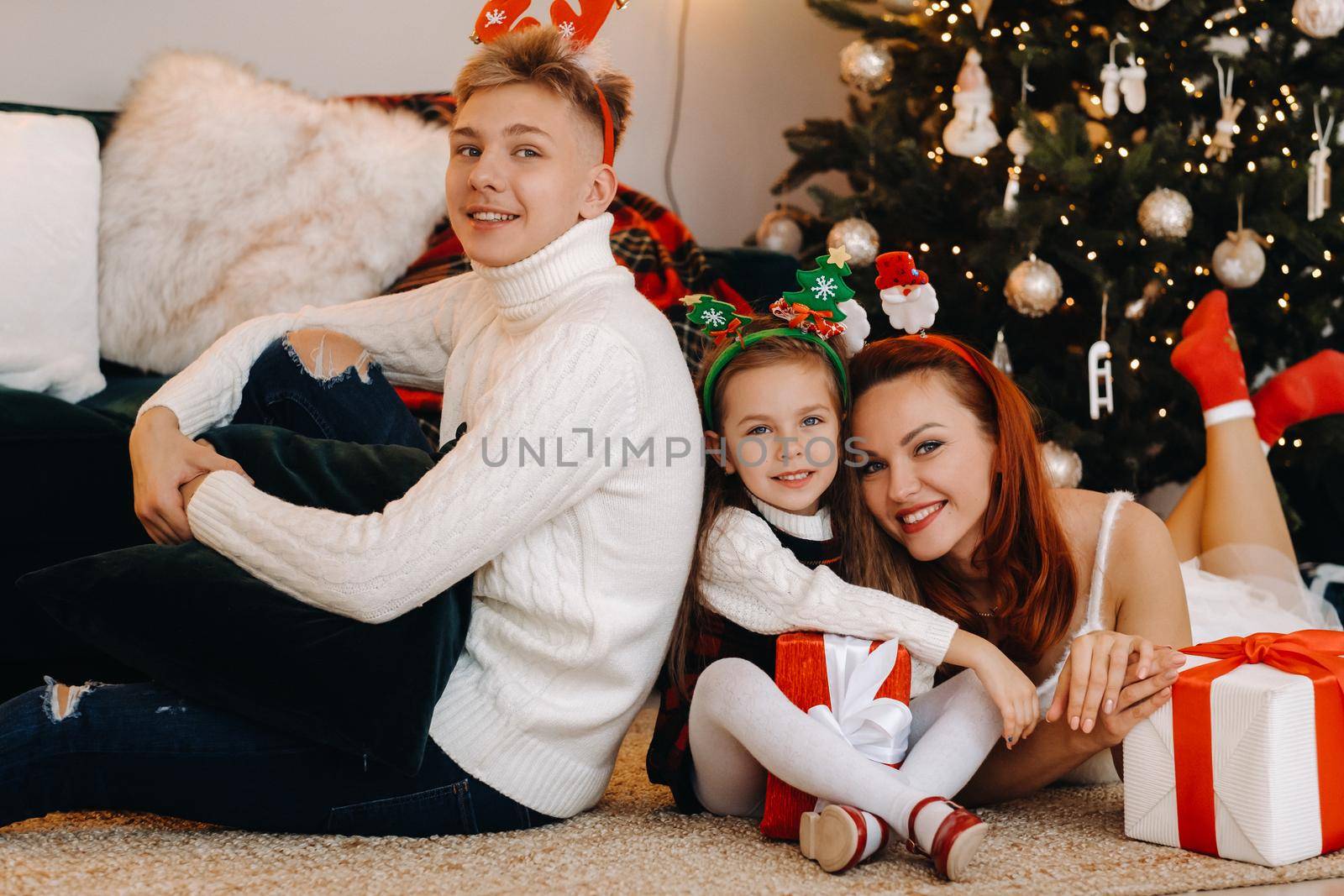 a happy family is lying on the floor of the house with New Year's gifts, next to the Christmas tree,