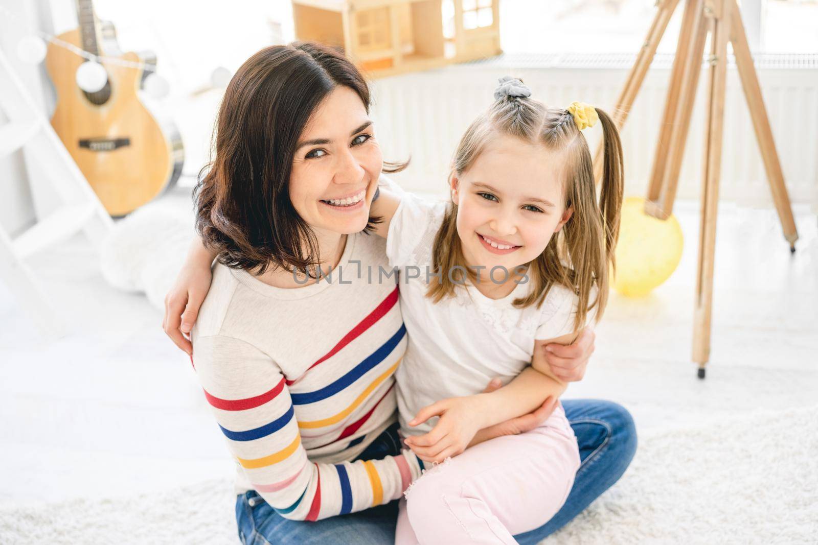 Cheerful little girl with lovely mother hugging in light room