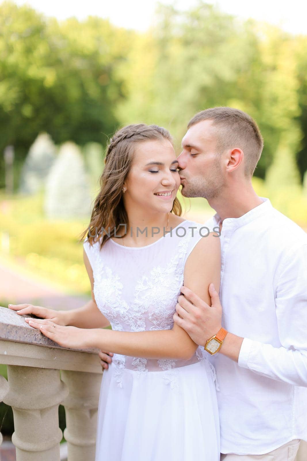 Happy beautiful bride and groom holding each other, kissing and standing outdoors. Concept of relationship, wedding and bridal photo session.