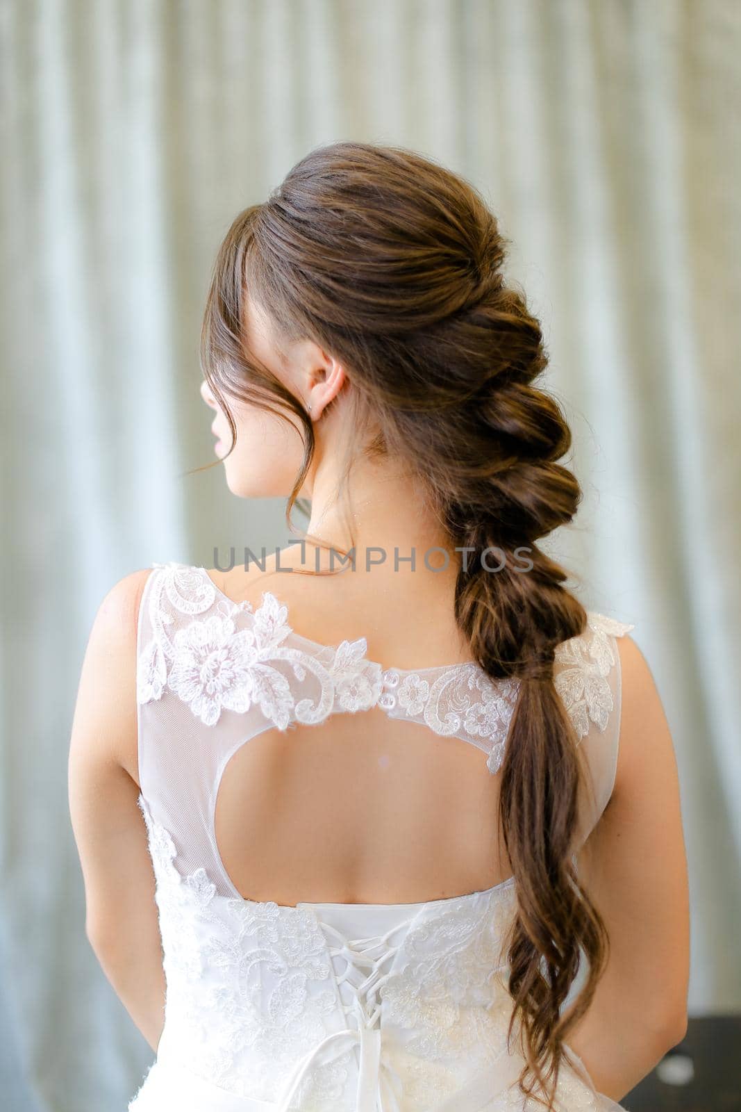 Back view of caucasian brunette bride with braid hair at studio. Concepf of bridal hair do and wedding.