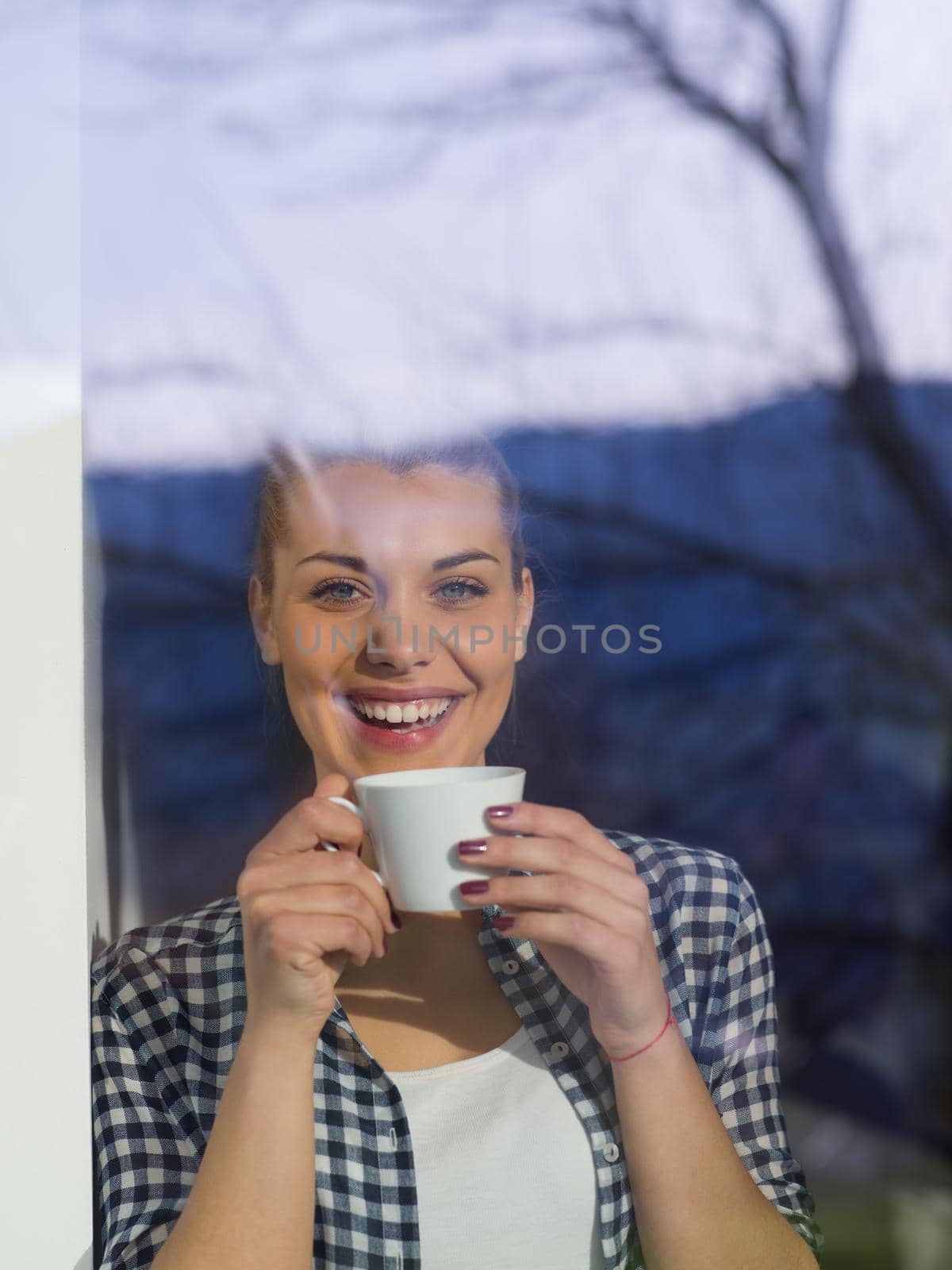 beautiful young woman drinking morning coffee by the window in her home