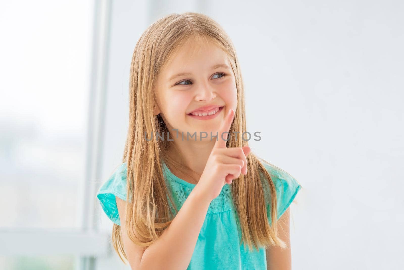 Portrait of adorable little girl in casual dress, smiling and showing one index finger