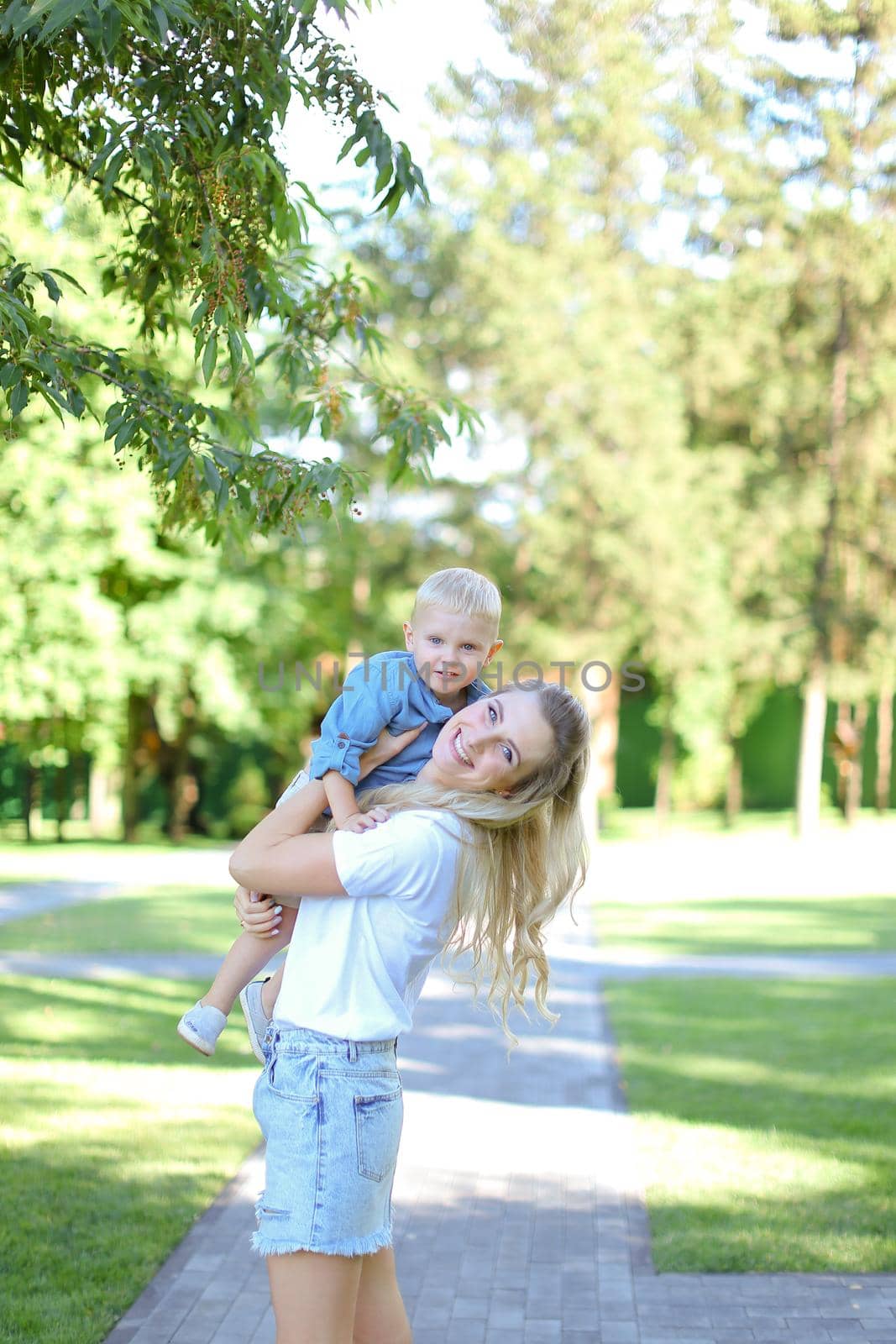 Young blonde mother playing with little son outside. Concept of motherhood and kids.