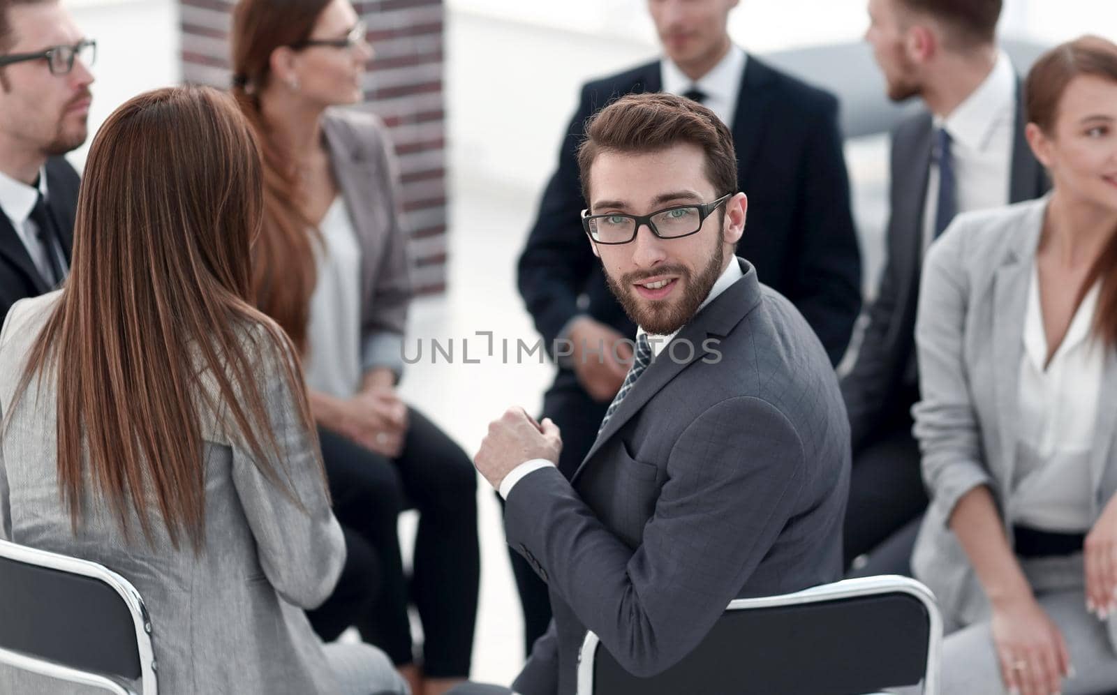 young employee sitting in a circle of colleagues and looking at the camera