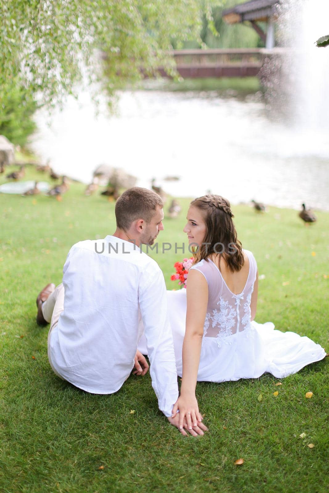 Handsome groom and bride sitting near lake and resting. Concept of married couple and nature.