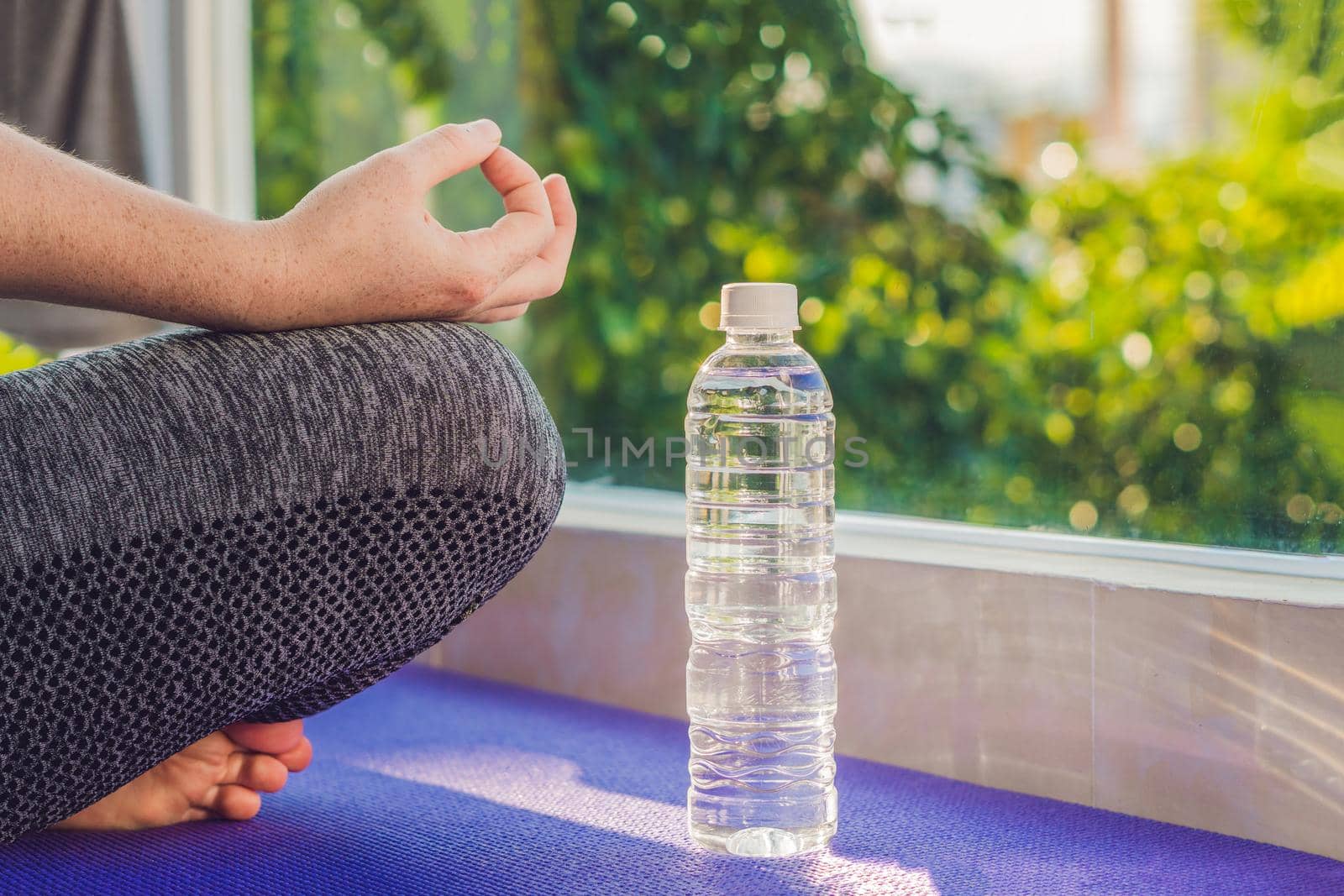 hand of a woman meditating in a yoga pose on a rug for yoga and a bottle of water.
