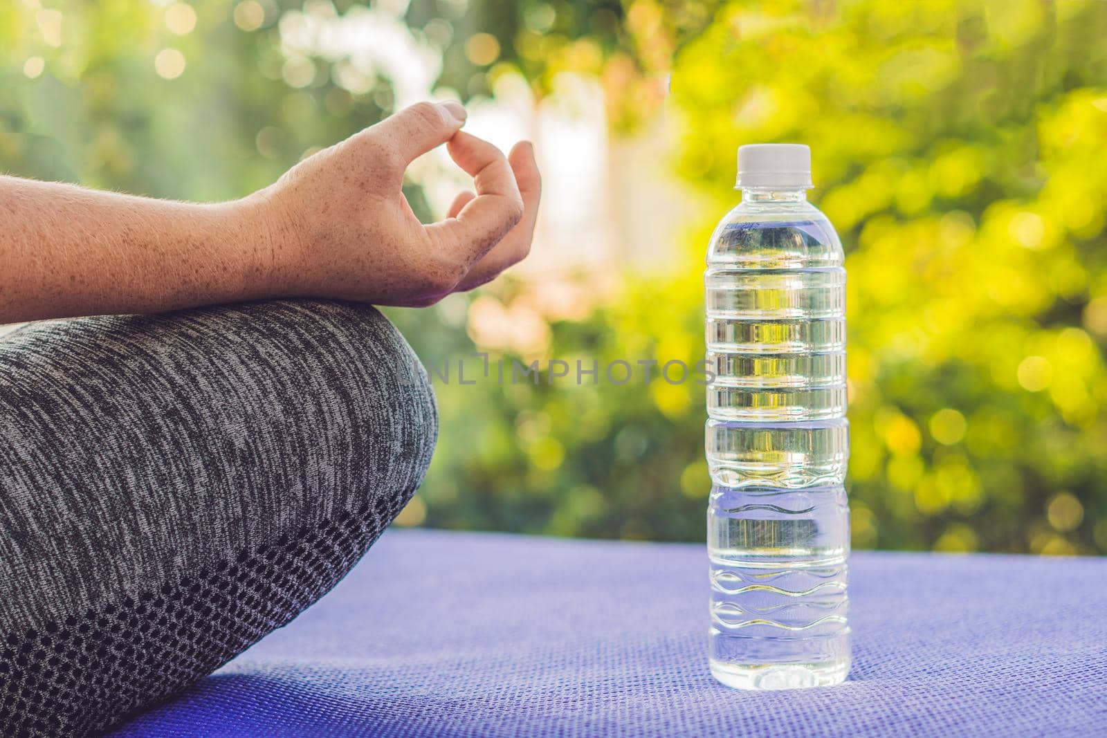 hand of a woman meditating in a yoga pose on a rug for yoga and a bottle of water by galitskaya