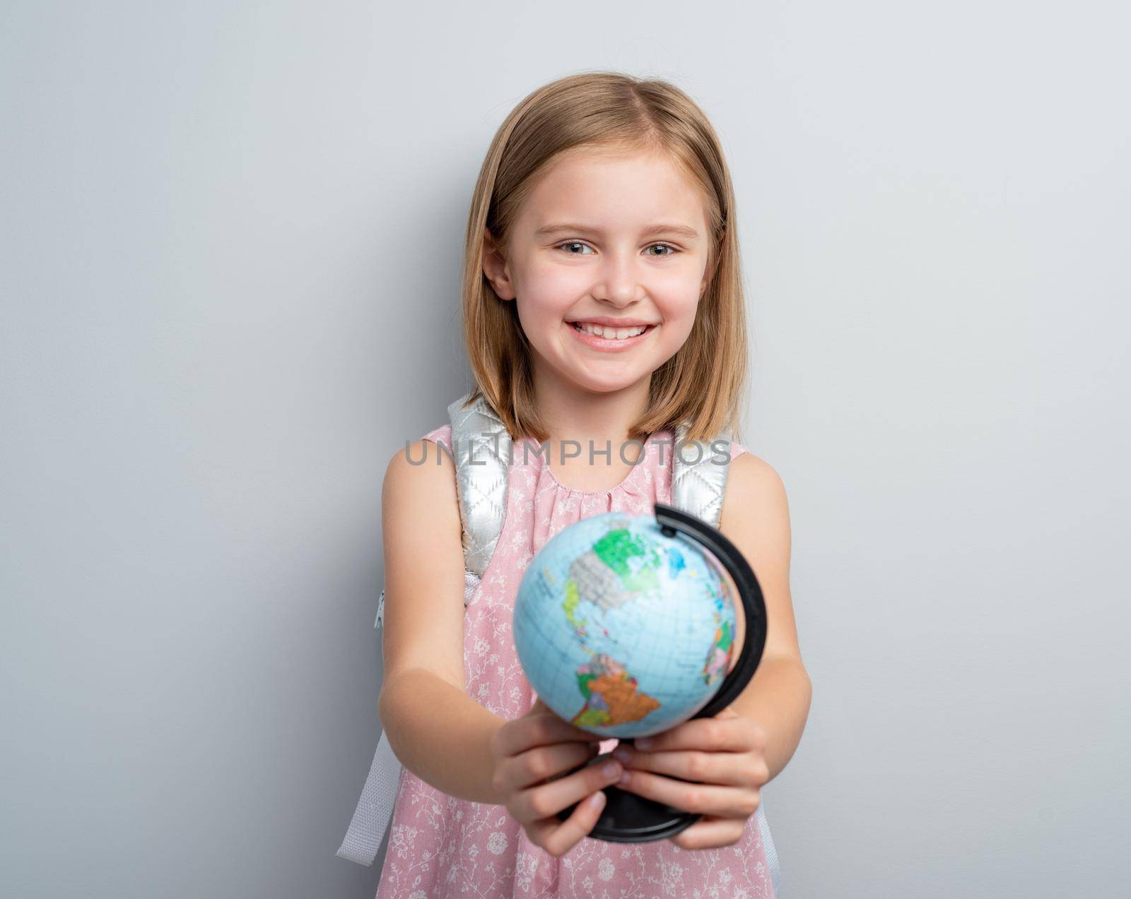 Schoolgirl holding small globe in front of her on gray background