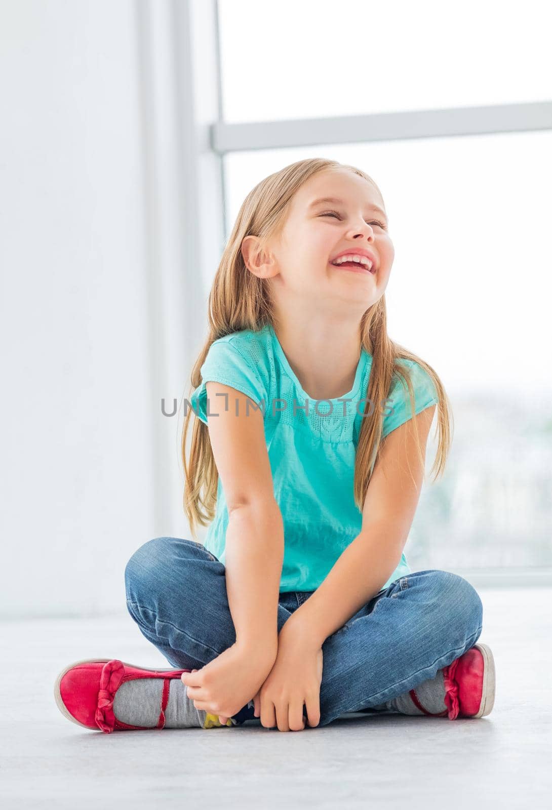 Blonde laughing little girl sits in light room.