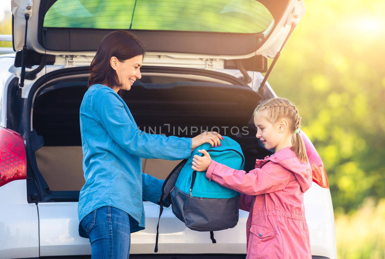 Mother giving backpack to daughter from car by GekaSkr