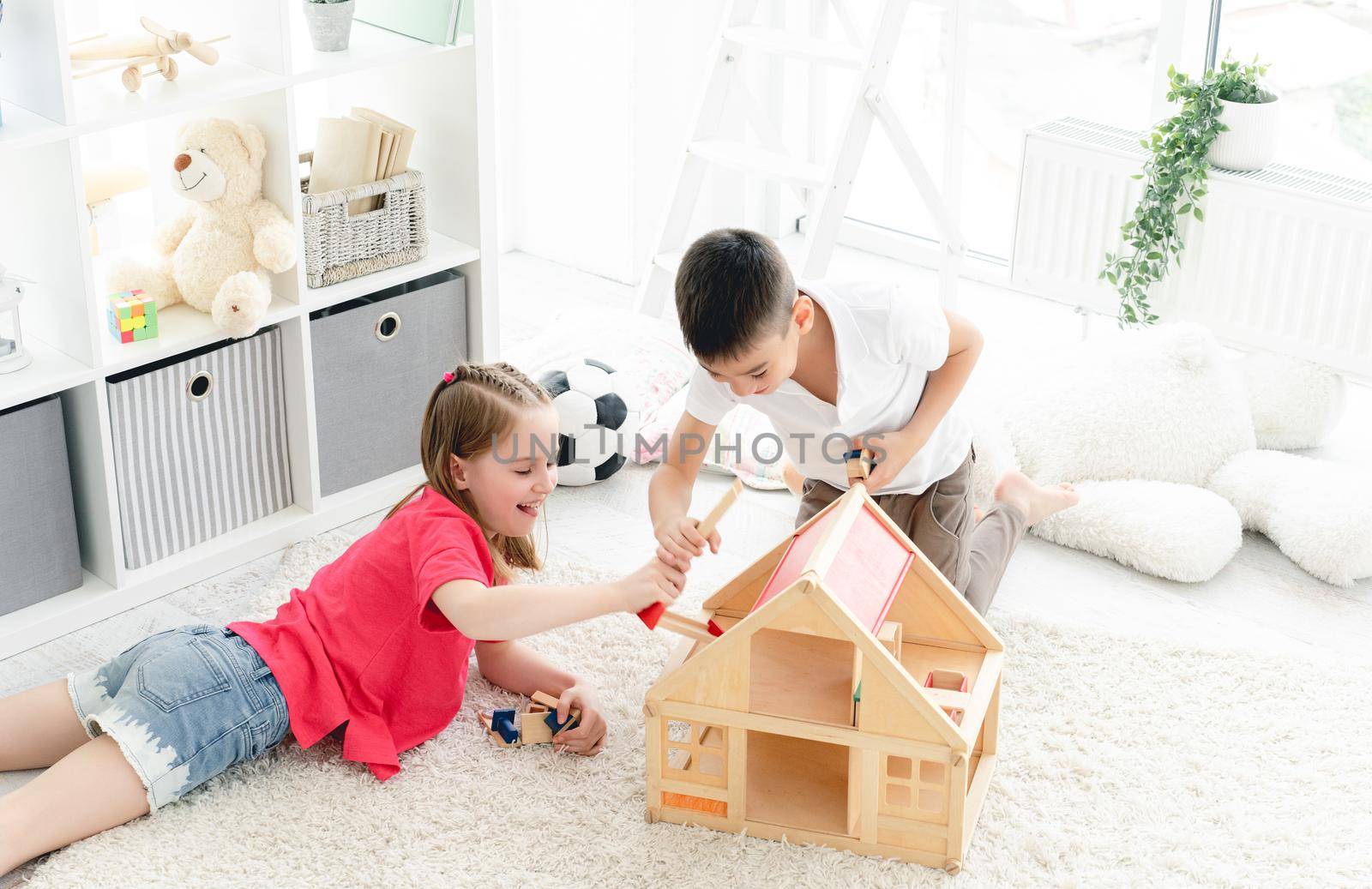 Smiling children playing with wooden wooden house in light room