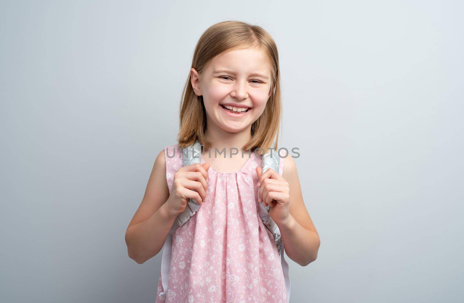 Smiling school girl with backpack on gray background