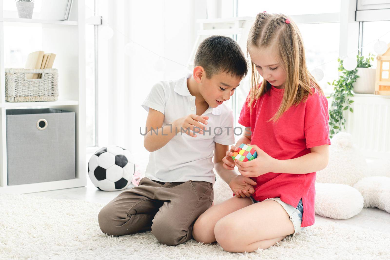 Cute girl and boy kids solving with rubik's cube in light room
