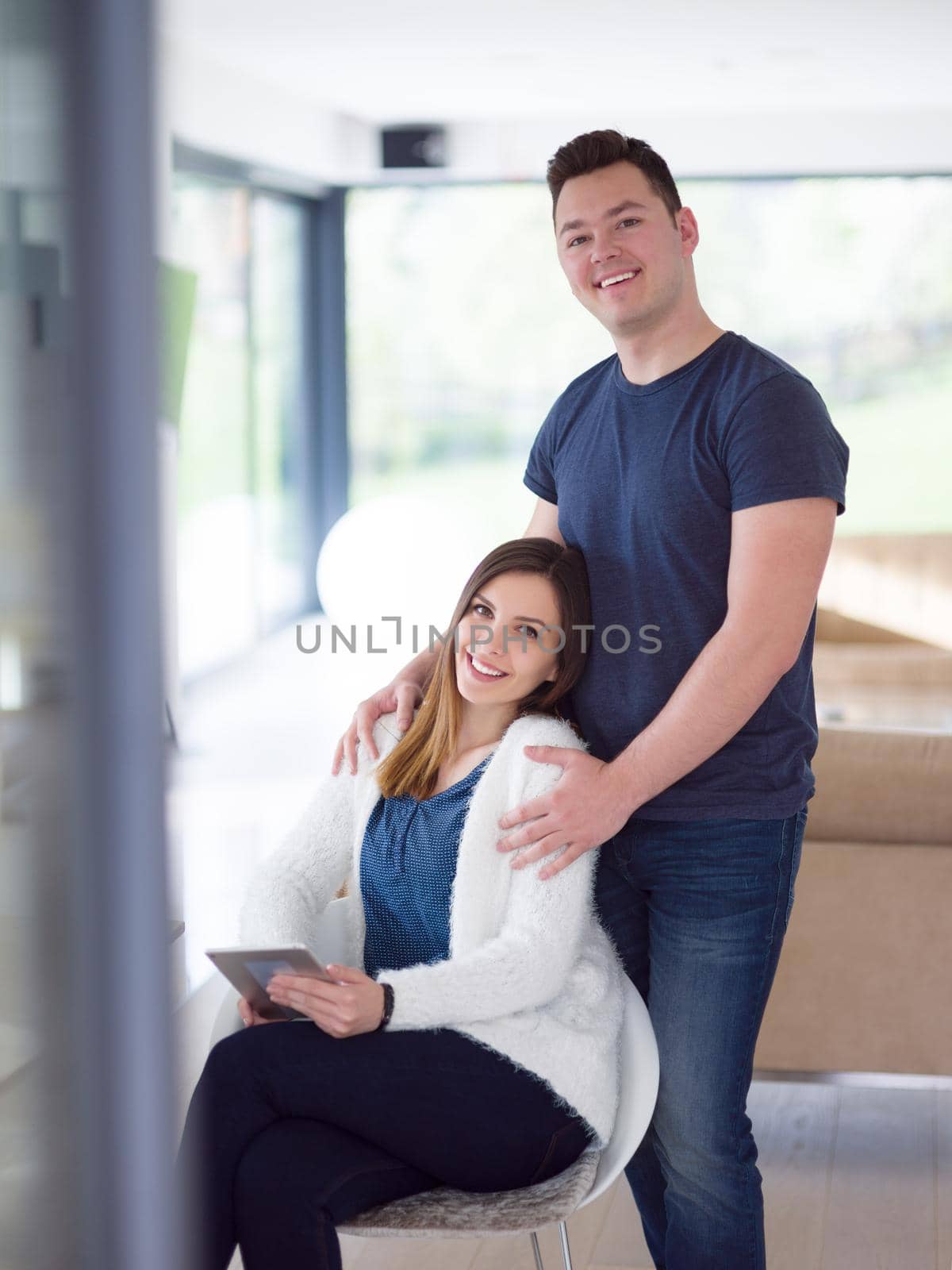 Young couple using tablet computer at luxury home together, looking at screen, smiling.