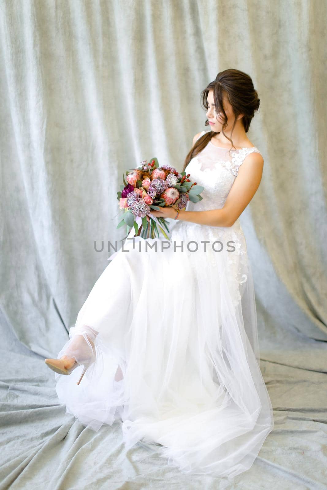 Photo of young bride sitting at studio with bouquet of flowers. by sisterspro