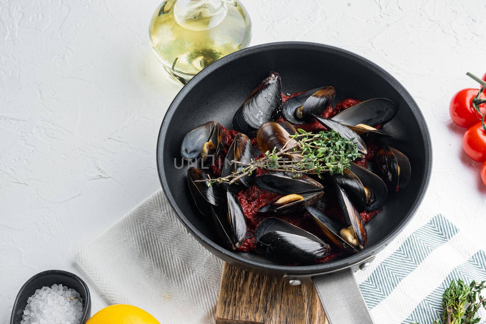 Mussels grilled with tomatoe sauce with herbs, on frying iron pan, on white background , with copyspace and space for text