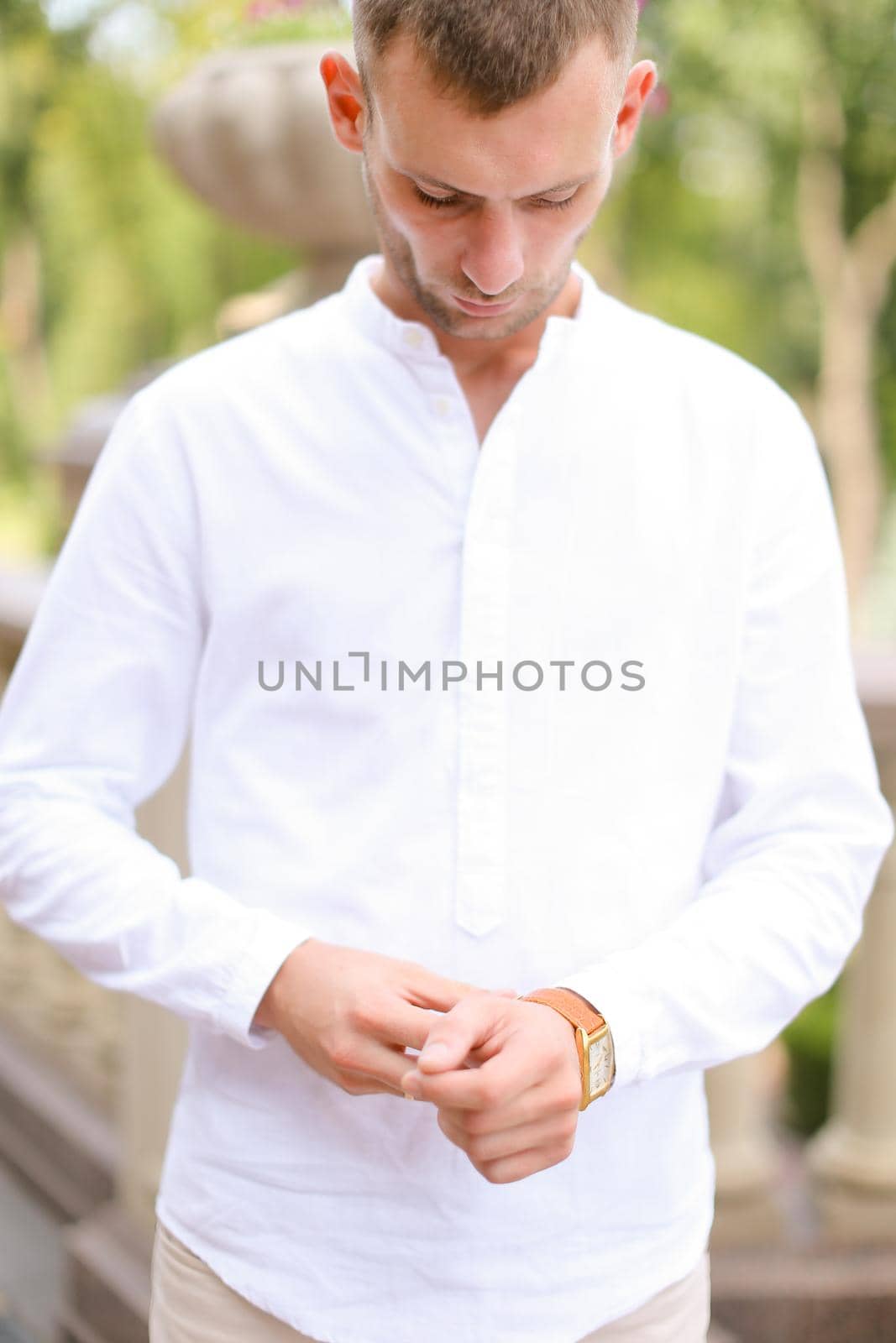 Caucasian young groom looking at watch and waiting for bride outside. Concept of bridal photo session and young man.