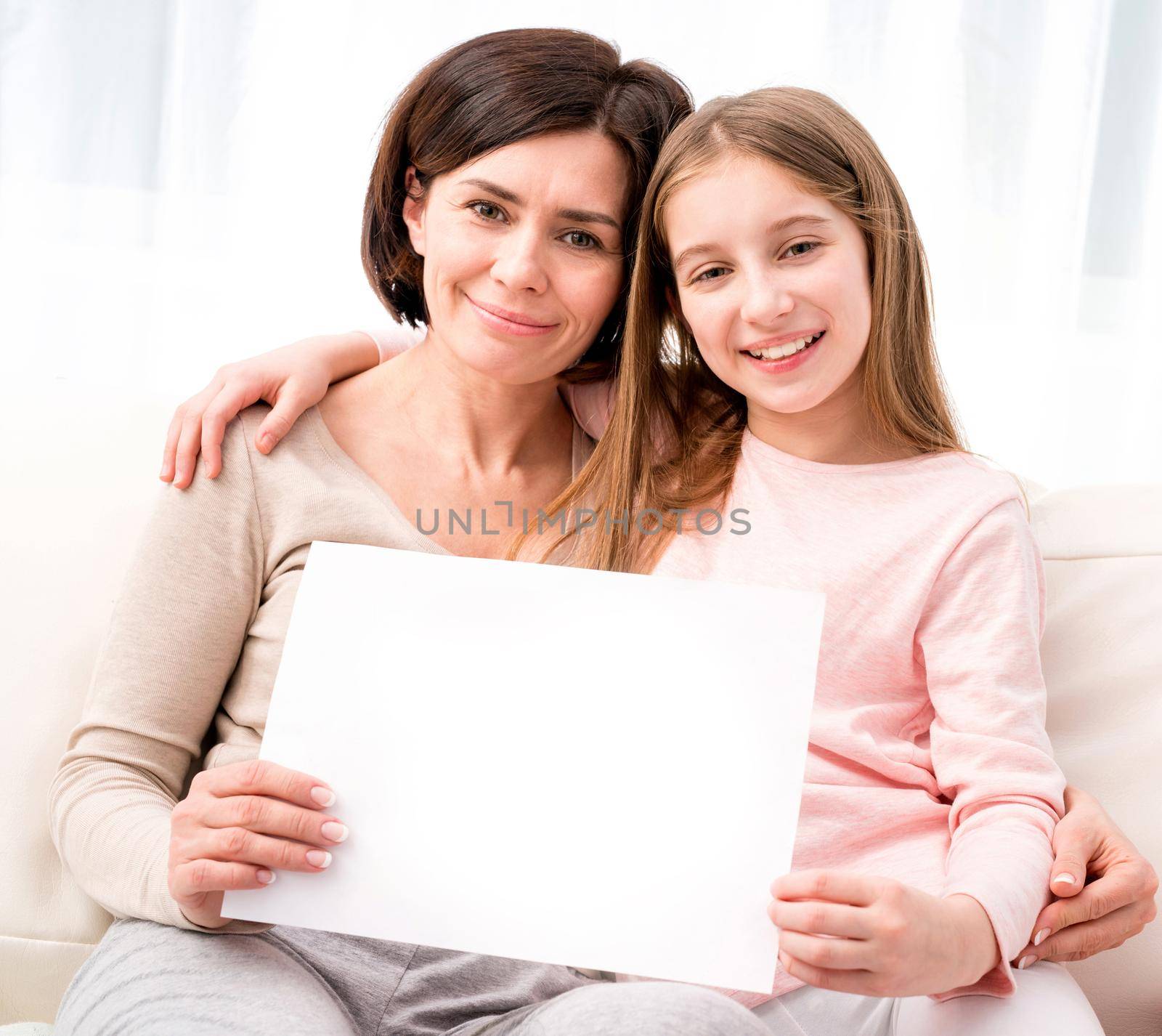Mother and daughter holding empty blank sheet of paper A4 in hands at home
